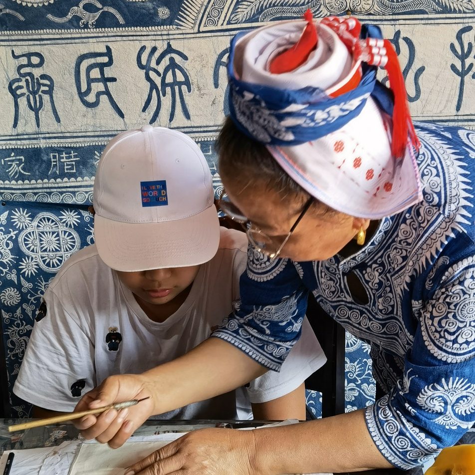 Students learning traditional handicraft techniques from local artisans in an ethnic minority village in China.